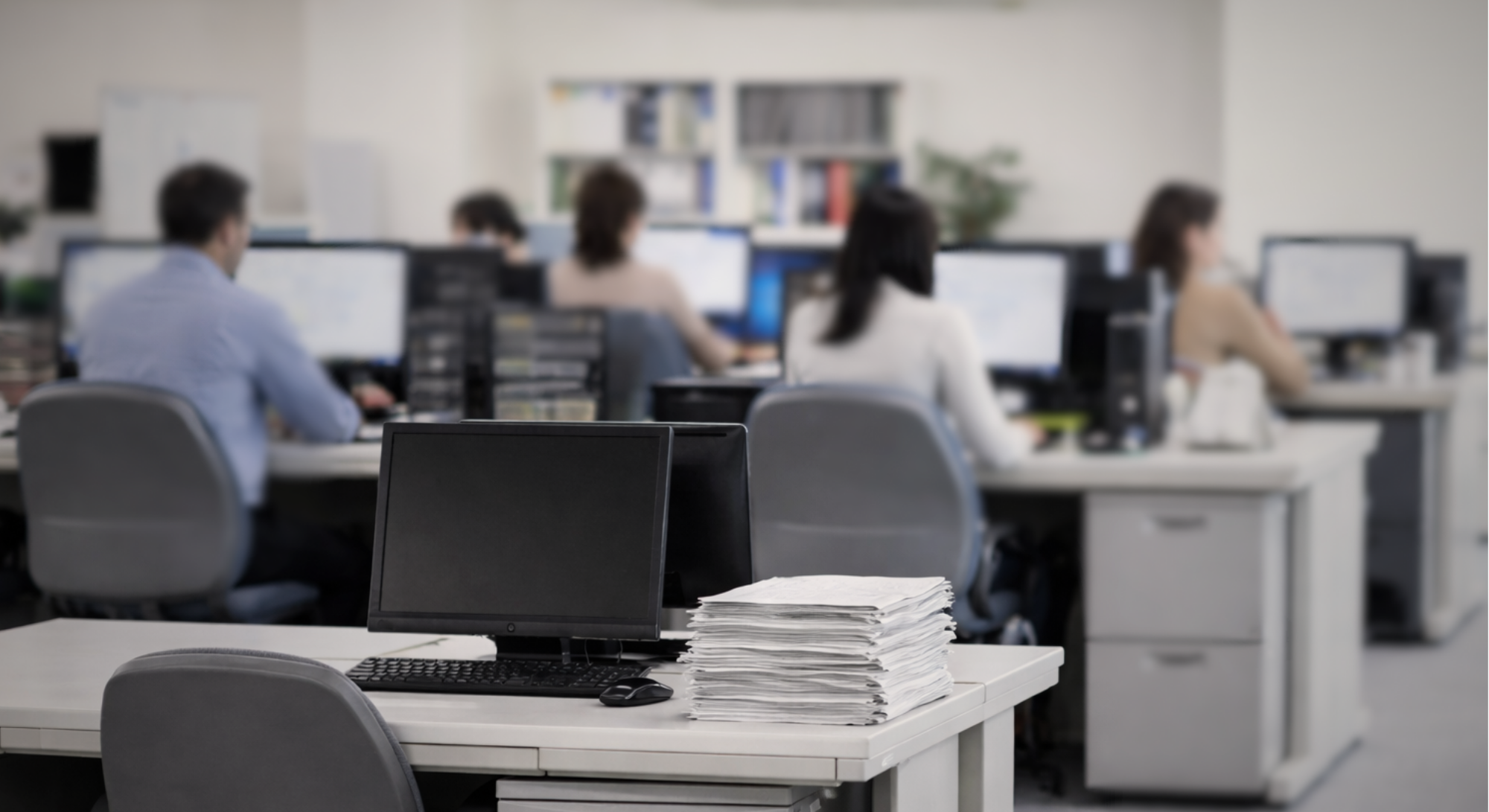 Mesa de escritório vazia em ambiente corporativo, com documentos acumulados, enquanto a operação da empresa continua ao fundo durante afastamento de colaborador.