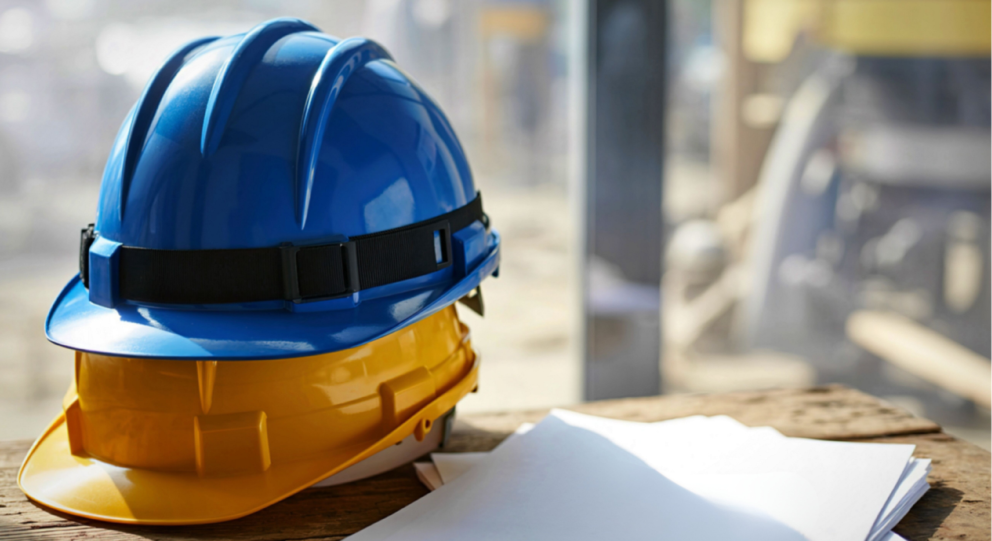 Capacetes de segurança sobre mesa em ambiente de obra, representando saúde e segurança do trabalho na adequação à NR-01